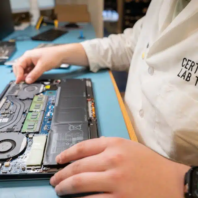 A disassembled laptop sitting on a blue desktop with hands holding it.