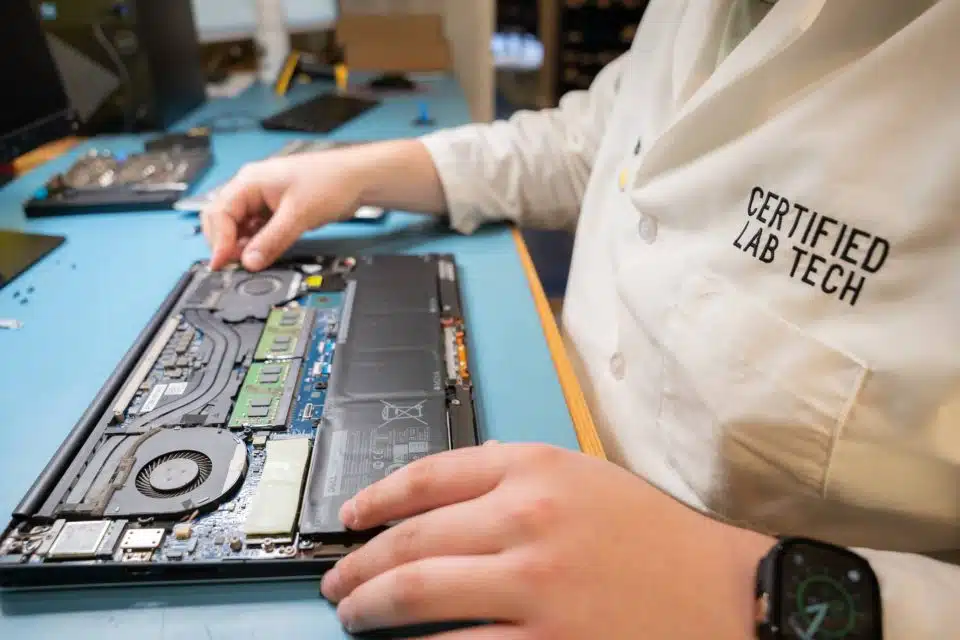 A disassembled laptop sitting on a blue desktop with hands holding it.