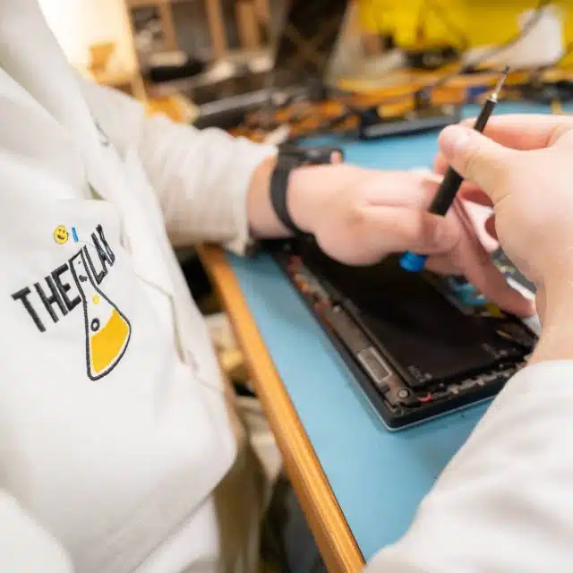 A repair tech using a screwdriver to repair the inside of a broken computer while wearing a white lab coat with The Lab logo on it.