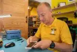 Lyle Schrock holding a broken iPhone while sitting at a blue desk wearing a yellow polo shirt with The Lab logo.