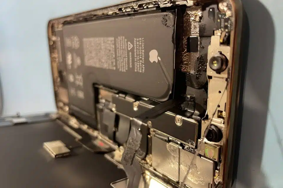 An iPhone that has been opened to show severe liquid damage on the inside of the device