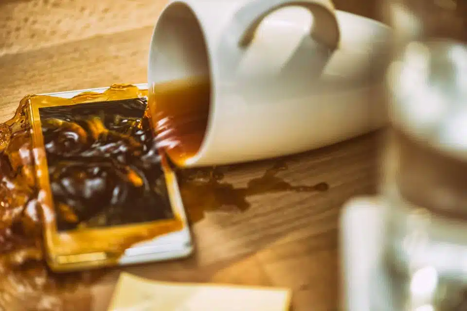 white coffee cup tipped over spilling coffee on a smartphone