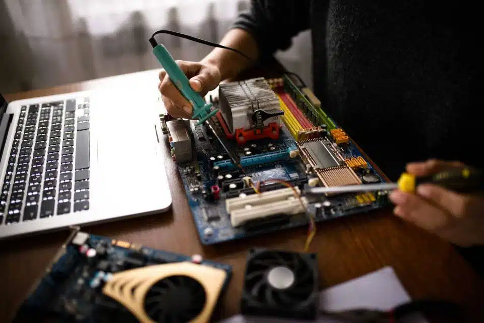 Hands using micro-soldering tools to complete computer repair on the interior of a laptop