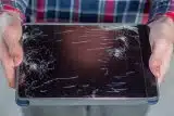 Hands holding a tablet with a cracked screen