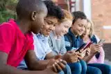 Five elementary-aged school children sitting and smiling as they look at their smartphones