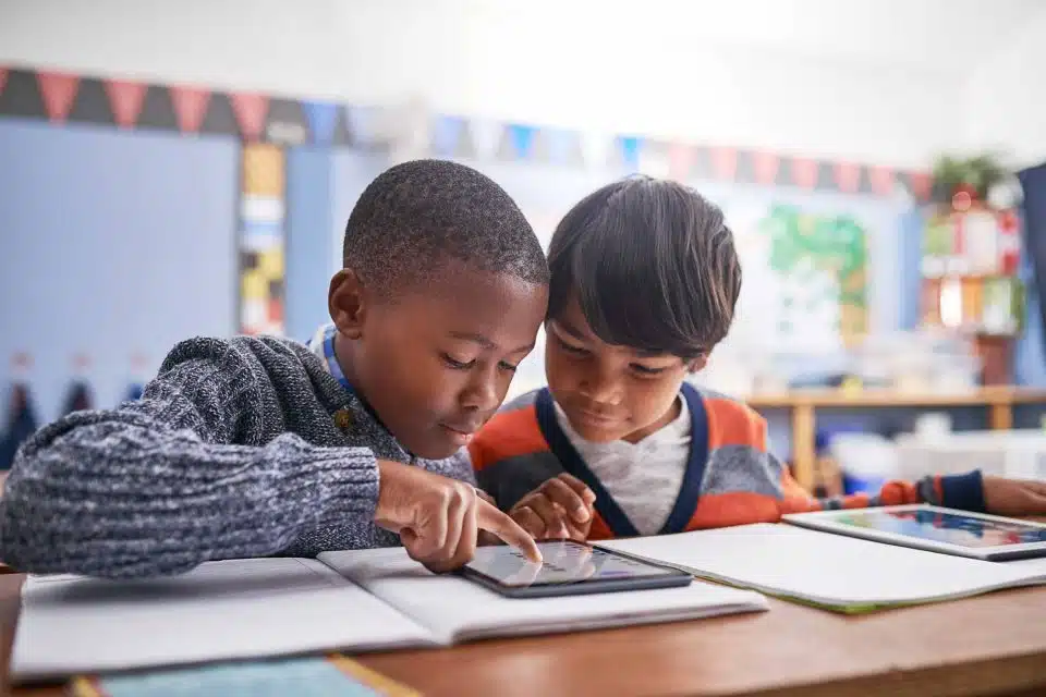 Two elementary-aged boys sitting in a classroom sharing a touch screen tablet