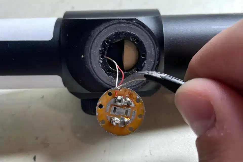 A hand using tweezers to repair a bowsight