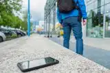 Person wearing a backpack walking away from a phone left on a city bench