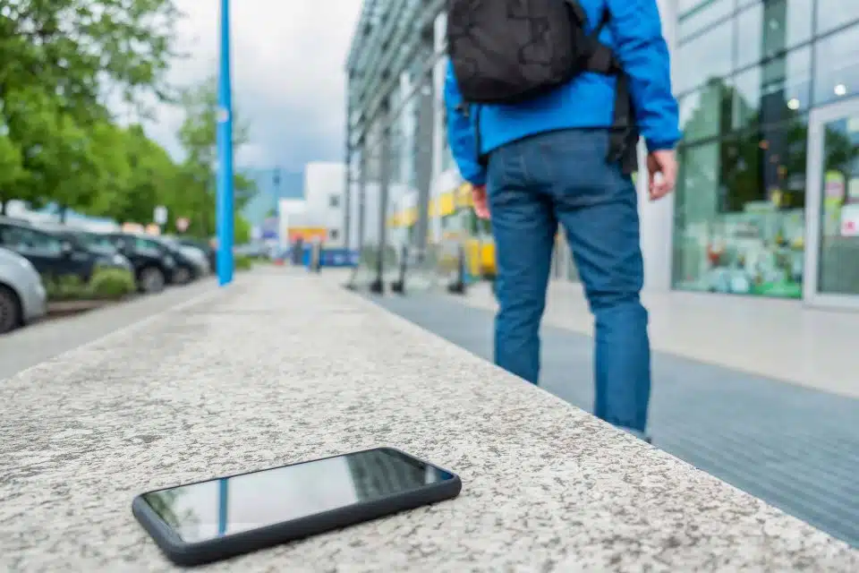 Person wearing a backpack walking away from a phone left on a city bench