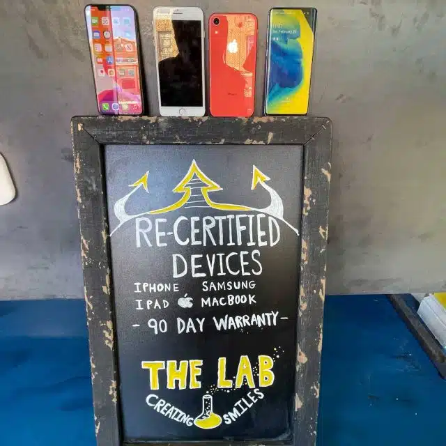 Re-certified, refurbished devices displayed on top of a sign at The Lab advertising a 90 day warranty