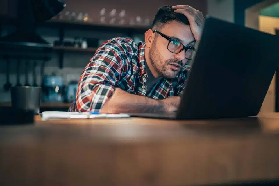 Man sitting in front of a laptop computer with his hand on his head looking frustrated and confused