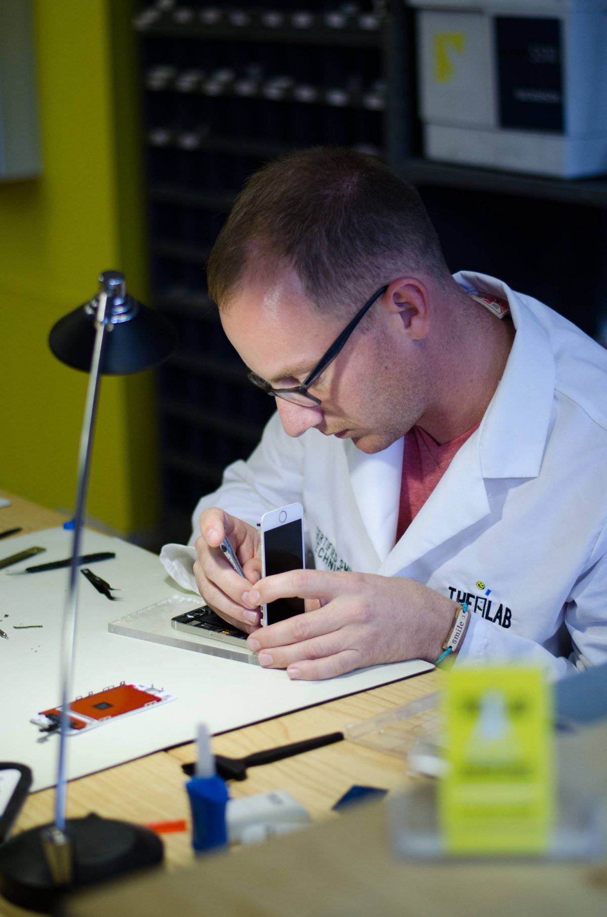 alt+"lyle schrock sitting at a table at the lab in warsaw fixing a cell phone screen