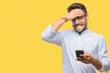 Man looking at the phone in his hand, frustrated with it with a bright yellow background