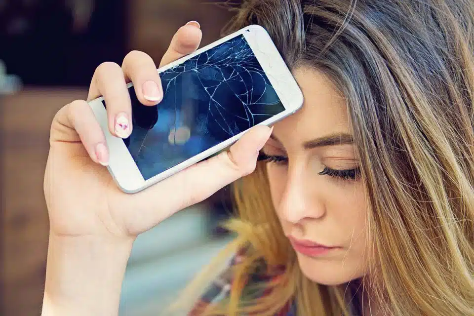 Woman holding her smartphone with a cracked screen against her head with a sad expression