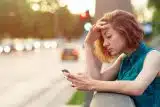 Woman with short, wavy red hair looking at her smartphone with an annoyed expression
