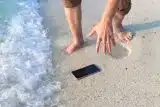 Smartphone dropped on the sand of a beach next to a wave coming in