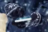 Someone wearing black gloves with white snowflakes using their touch screen smartphone in the winter