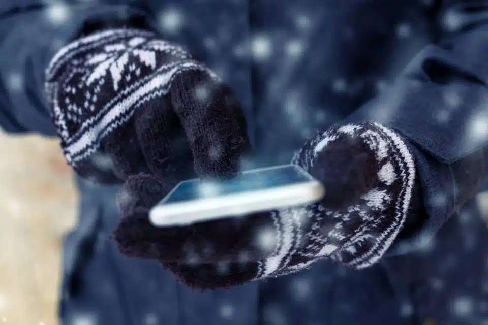Someone wearing black gloves with white snowflakes using their touch screen smartphone in the winter